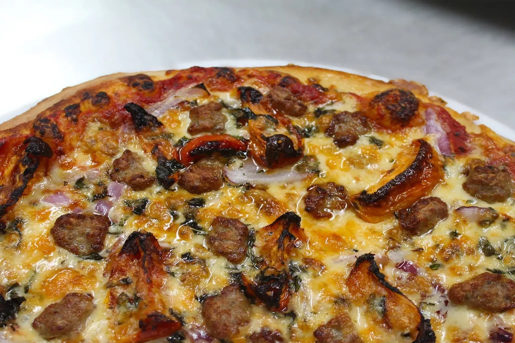 Freshly baked pizza with sausage, melted cheese, red peppers, and onions.
