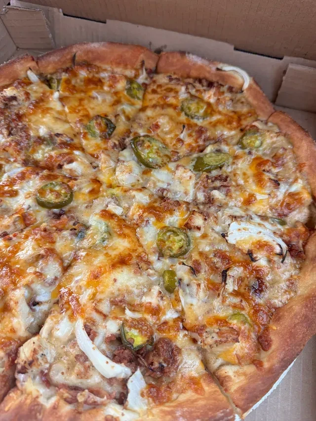 Pizza with melted cheese, jalapeños, onion, and chicken in a pizza box.
