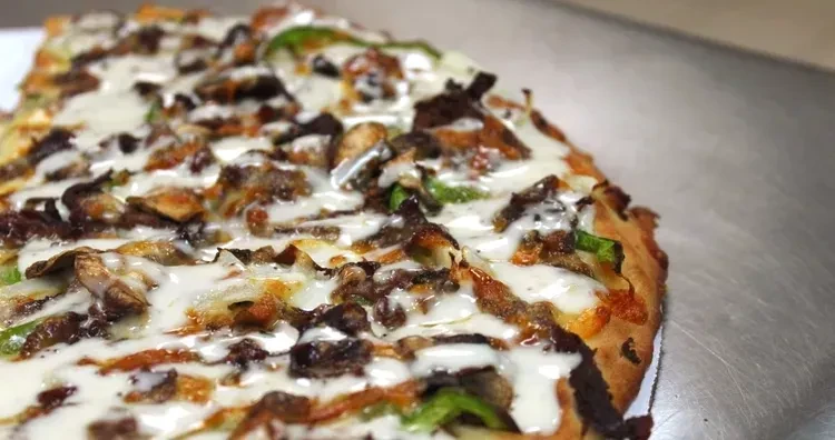 Close-up pizza slice topped with meat, green peppers, and melted cheese.