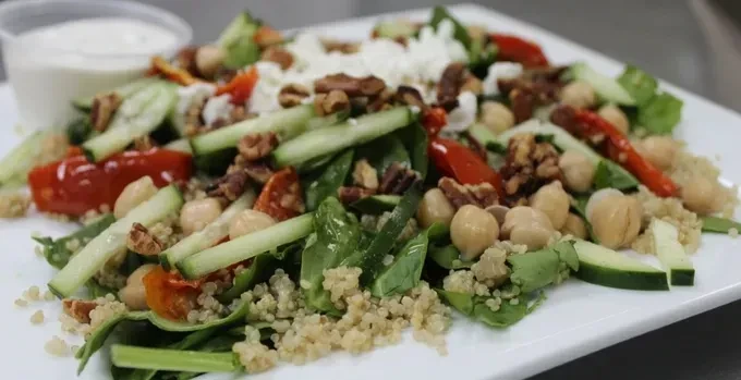 Colorful salad with spinach, cucumber, tomatoes, chickpeas, quinoa, feta, nuts.