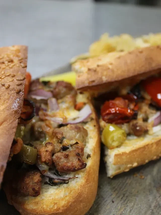Sub sandwich halves loaded with browned meat, melted cheese, and vegetables.