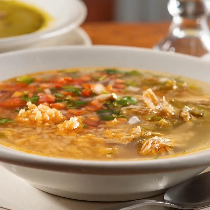 Steaming bowl of chicken and rice soup with vegetables and herbs.