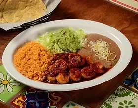 Mexican plate with shrimp, rice, guacamole, and beans on colorful tiles.