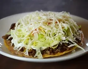 Close-up of a tostada with beans, lettuce, crema, and shredded cheese.