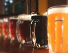 Close-up of a row of foamy beer mugs, dark stout in focus.