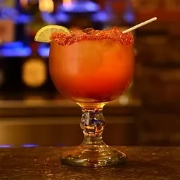 Amber cocktail in a goblet with a chili-salted rim, lime garnish, and white straw.