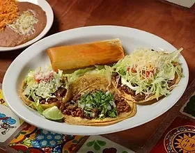 Mexican food platter with three tacos, tamale, refried beans, and rice.