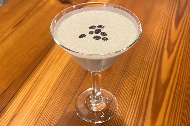 Light creamy cocktail in martini glass, garnished with whole coffee beans.