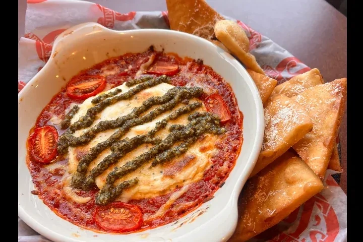 Baked tomato-cheese dip with pesto, cherry tomatoes, served with fried chips.