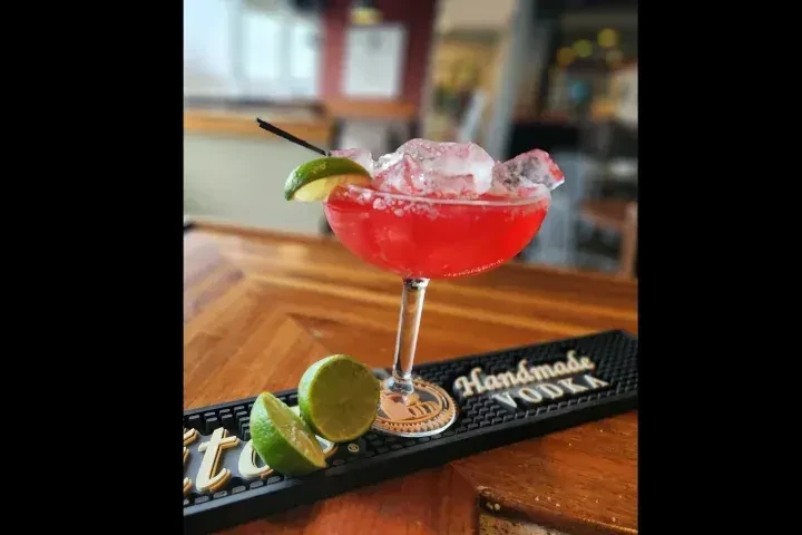 Vibrant red cocktail with crushed ice, lime on herringbone bar.