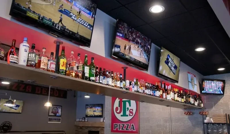 Stocked bar shelf, multiple TVs showing March Madness, and pizza signs.