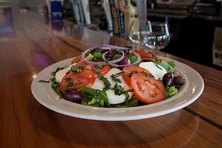 Plate of fresh salad with tomatoes, mozzarella, basil, and olives.