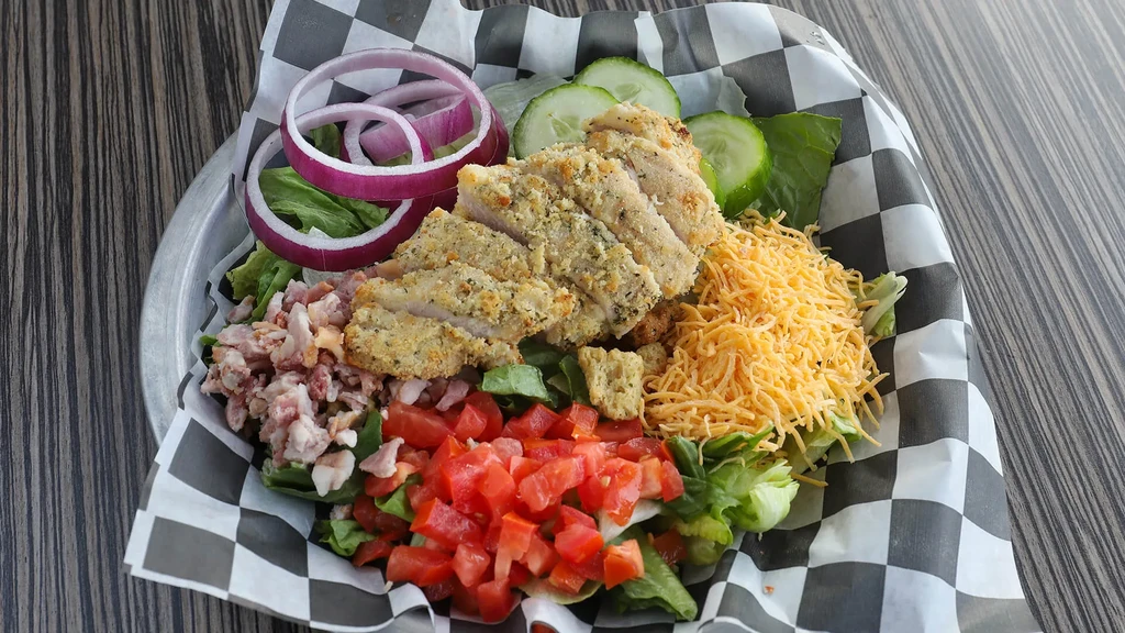 Vibrant salad with breaded chicken, cheese, bacon, and fresh vegetables.