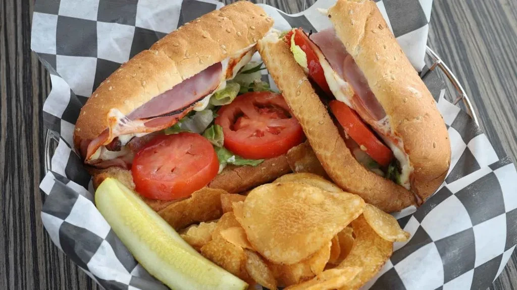 Deli sandwich, potato chips, and pickle in a checkered basket.