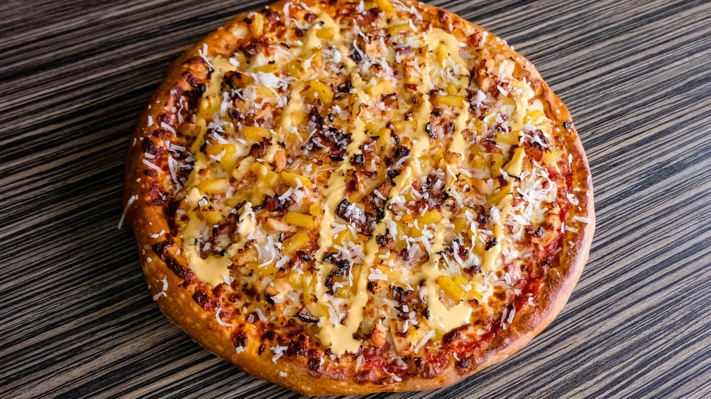 Pizza with pineapple, crispy meat, white flakes, and creamy yellow sauce.