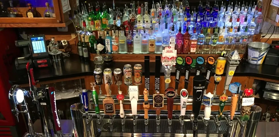 Numerous beer taps and colorful, illuminated liquor bottles behind a bar.