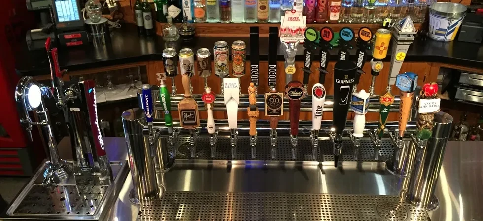 A well-stocked bar counter displaying many beer taps and liquor bottles.