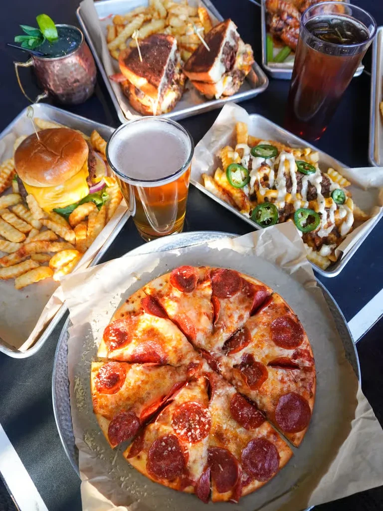 Overhead view of a casual meal with pizza, burgers, fries, wings, drinks.