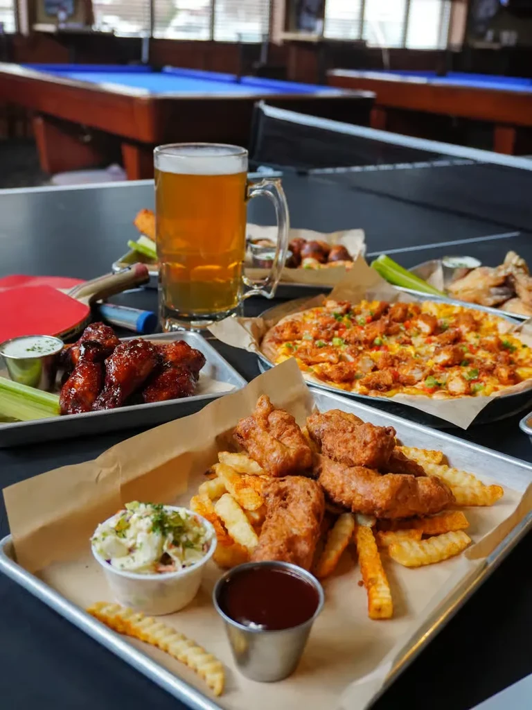 Fried chicken, wings, pizza, and beer on trays at a game venue.