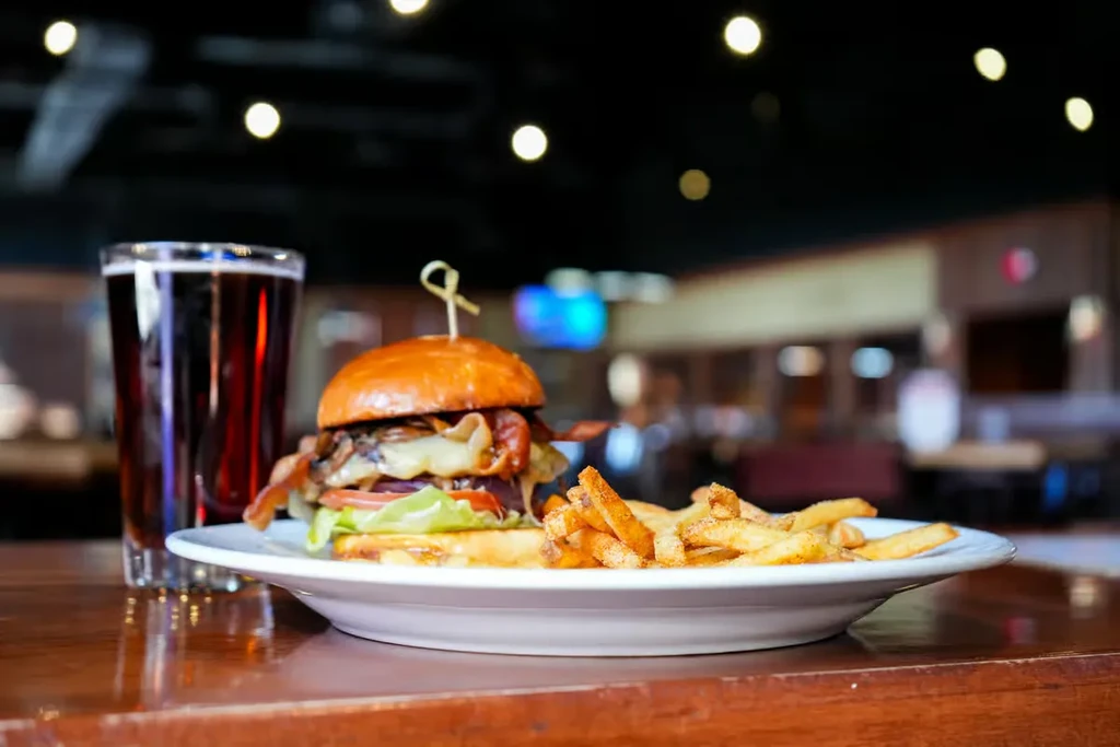 Gourmet burger, seasoned fries, and a dark drink on a wooden table.