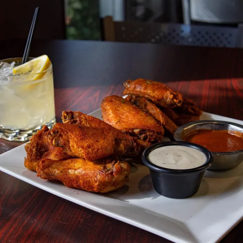 Plate of crispy fried chicken wings, dipping sauces, and a lemon cocktail.