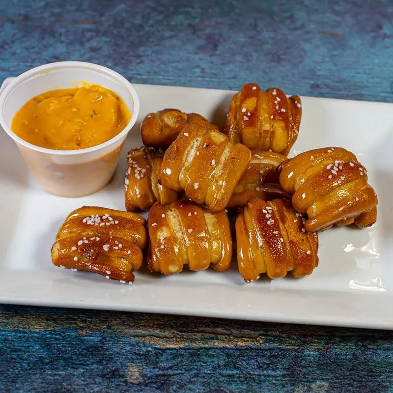 Glossy salted pretzel bites with cheese/mustard sauce on white plate.