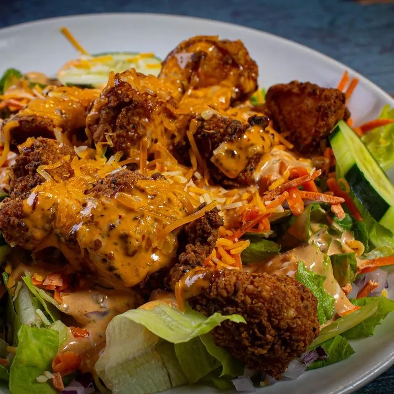 Vibrant salad with fried protein, vegetables, creamy dressing, and cheese.