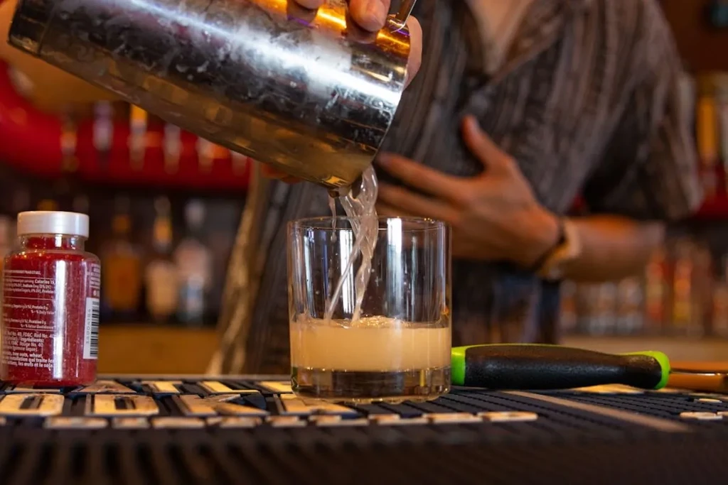 Bartender vigorously pours a drink from a shaker into a glass.