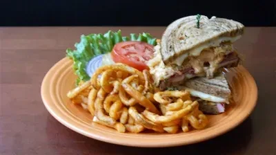 Orange plate with a stacked sandwich, curly fries, and vegetable garnish.