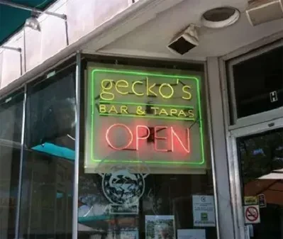 Prominent yellow-green and red neon 'gecko's BAR & TAPAS OPEN' sign.