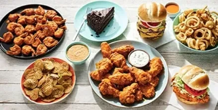 Overhead flat-lay of fried chicken, shrimp, burgers, fries, and cake.