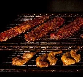 Seasoned ribs and chicken halves cooking on a metal grill.