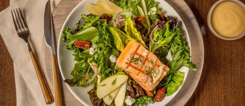 Plated grilled salmon salad with greens, apple, pecans, and cheese.