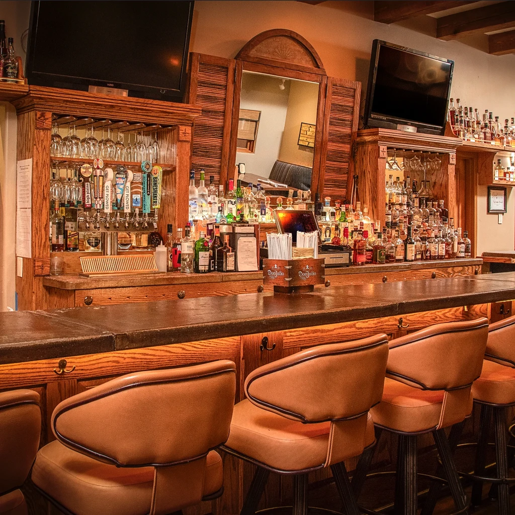Empty restaurant bar with dark counter and elaborate wooden back bar.