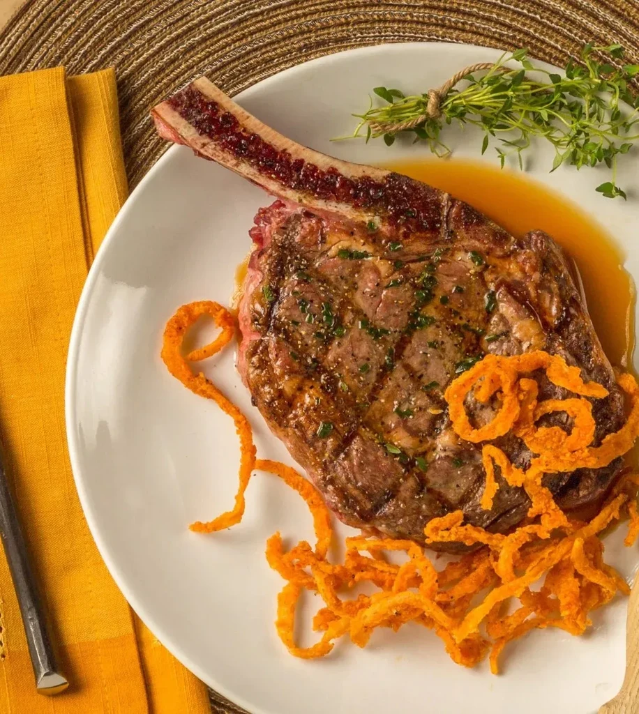 Grilled tomahawk steak with bone marrow, fried onion strings, and fresh herbs.