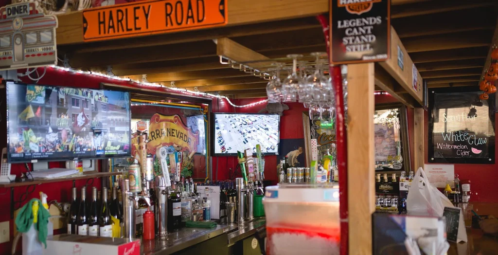 Well-stocked bar, TVs showing sports, Harley decor, and fall pumpkins.