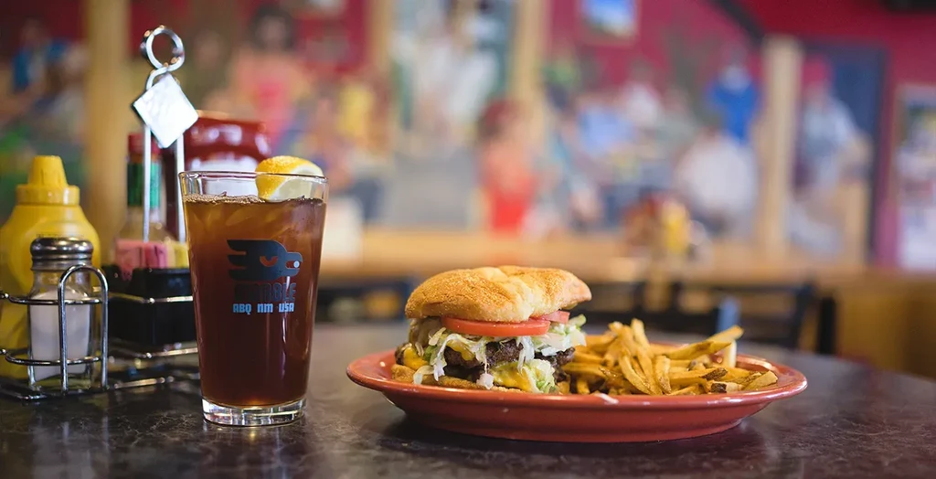 Double-patty burger, fries, iced tea, and condiments on a dark table.