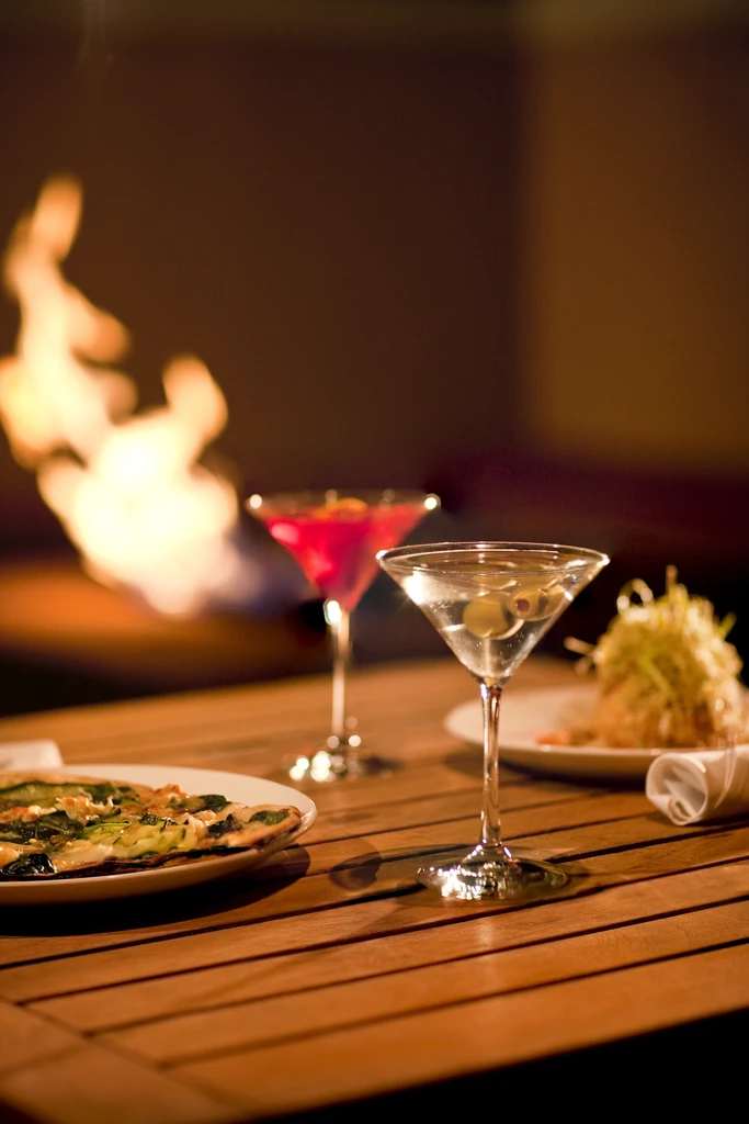 Food, cocktails, and napkin on a wooden table with fire background.