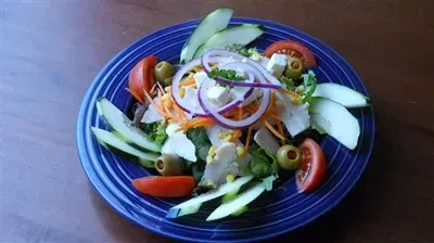 Mixed green salad with chicken, vegetables, and feta on a blue plate.