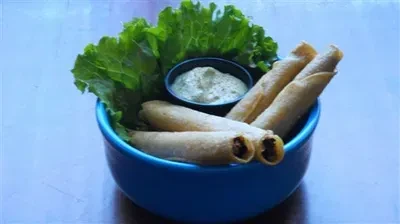 Golden taquitos, green dip, and fresh lettuce in blue bowl.