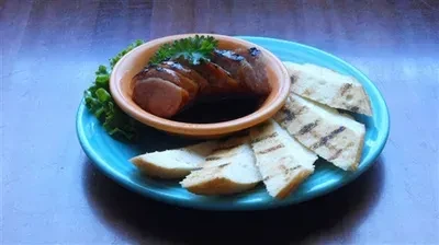 Grilled sausage in dark sauce with grilled bread and parsley.