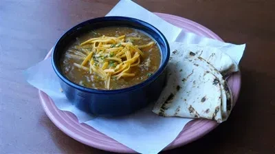 Dark blue bowl of cheesy soup with herbs and two tortillas.