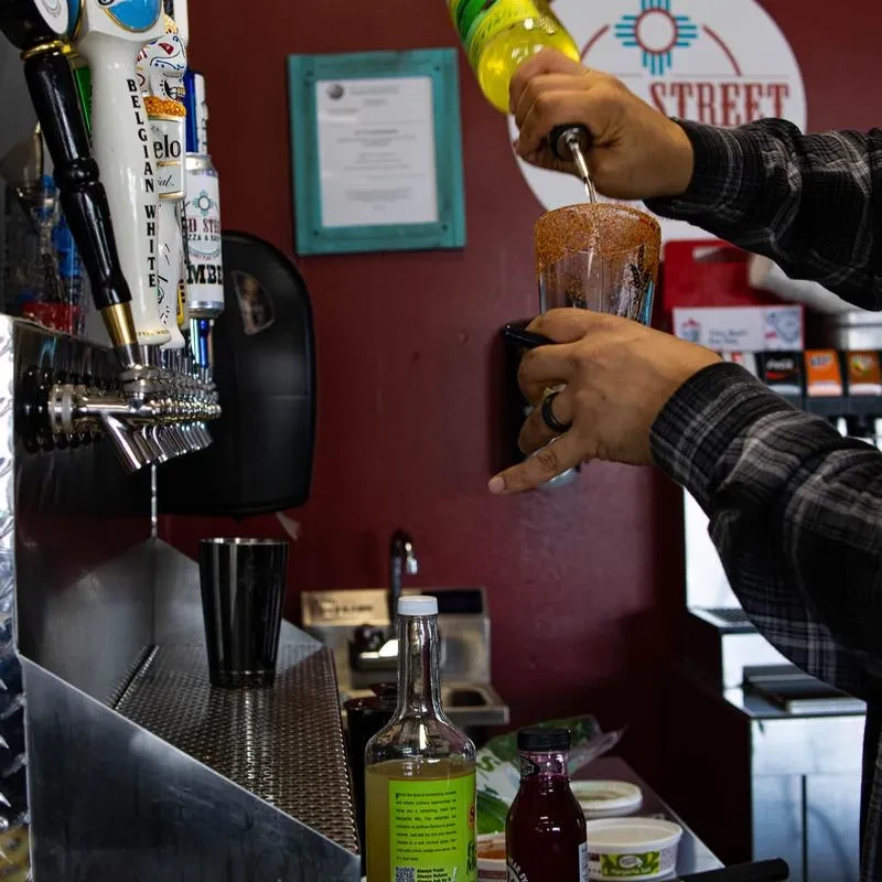Hands pouring yellow liquid into a spiced-rimmed glass behind a bar.