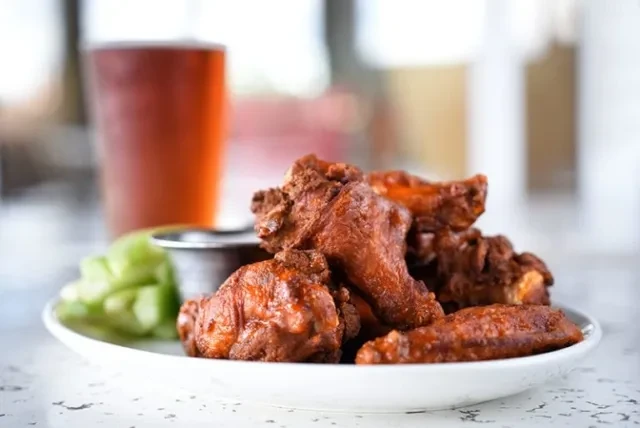Spicy chicken wings with celery sticks and dipping sauce on a plate.