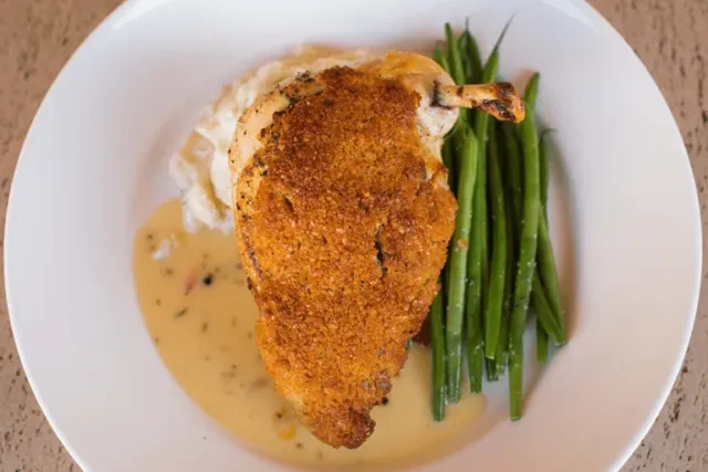 Professionally plated breaded chicken, mashed potatoes, green beans, and creamy sauce.