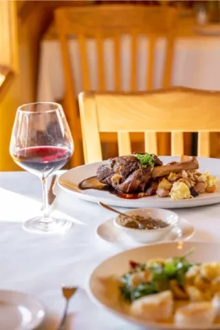Lamb shank, roasted vegetables, red wine on a restaurant table.