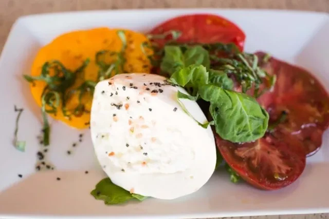 Fresh mozzarella, black sesame, pink salt, colorful heirloom tomatoes, and basil.