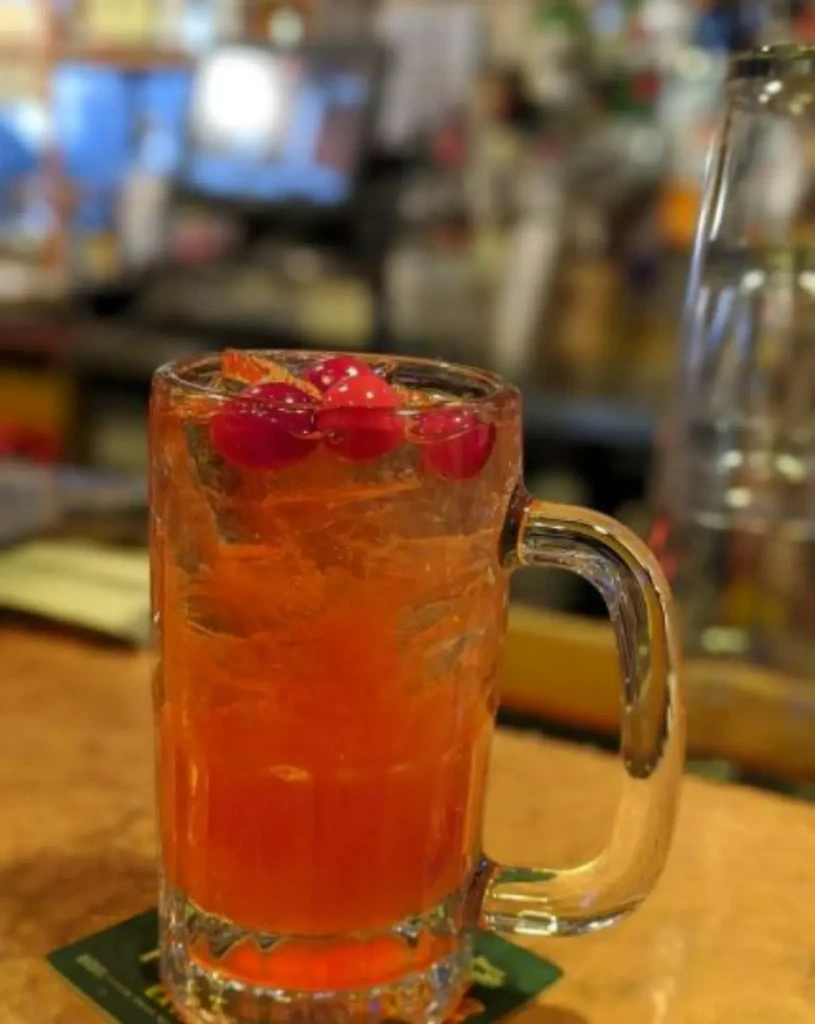 Vibrant reddish-orange drink with ice and cranberries in a clear mug.