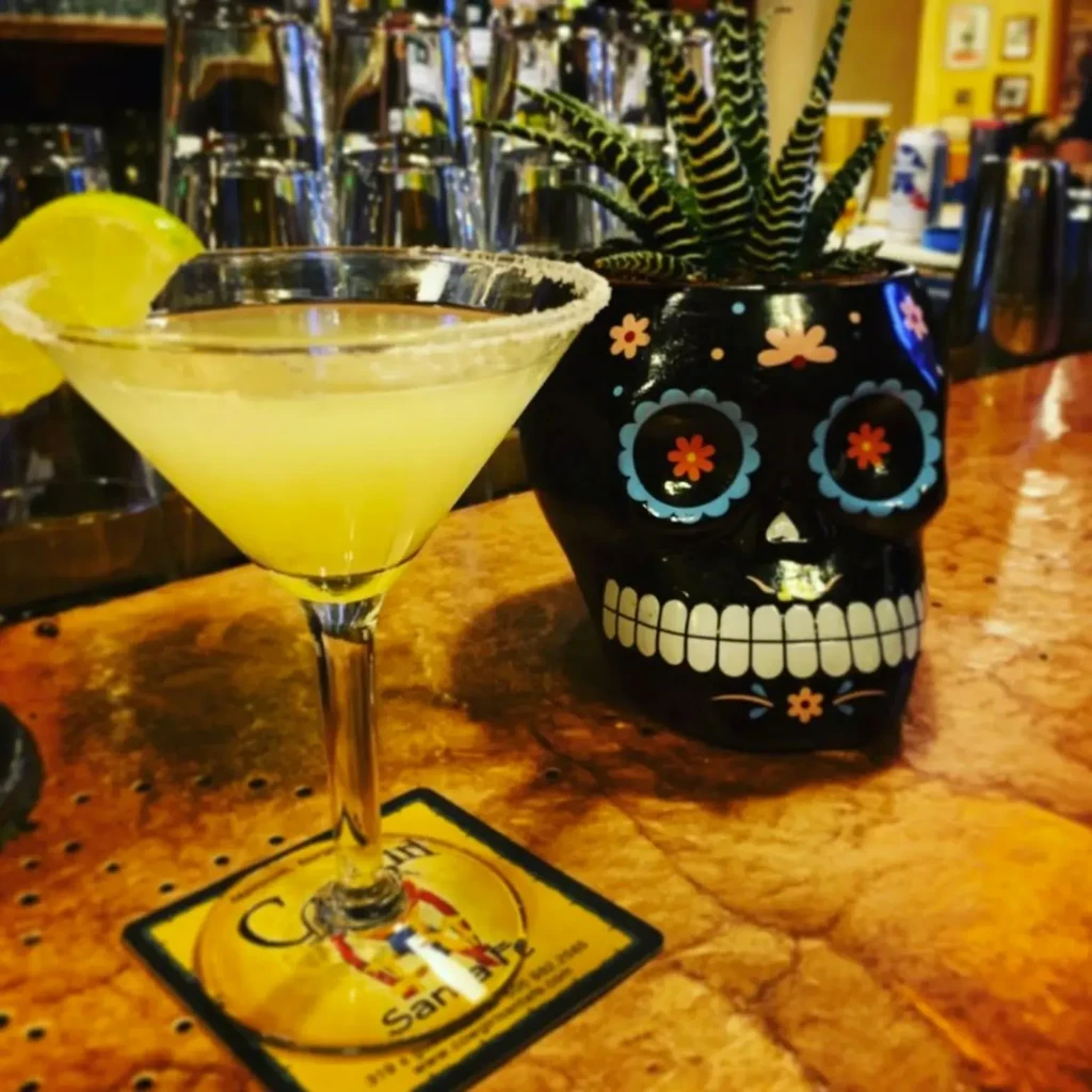 Salt-rimmed martini with lime, next to a Día de los Muertos skull planter.