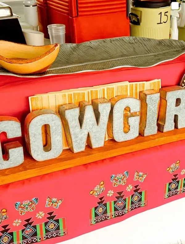 COWGIRL sign on a counter with a red patterned tablecloth.
